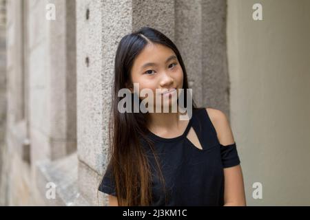 Ritratto di una ragazzina che si appoggia contro un muro di pietra; Hong Kong, Cina Foto Stock