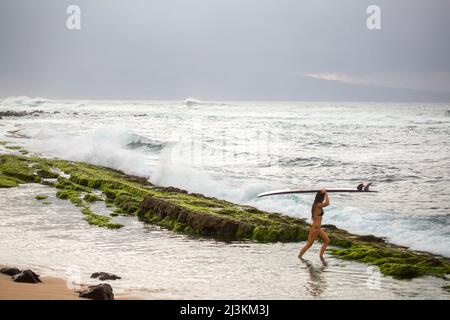 Un surfista professionista porta la sua tavola da surf verso le onde. Foto Stock