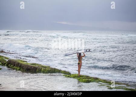 Un surfista professionista porta la sua tavola da surf verso le onde. Foto Stock