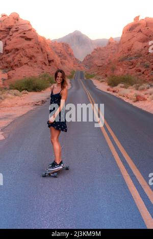 Una donna scivola lungo una strada desertica vuota nel Valley of Fire state Park. Foto Stock