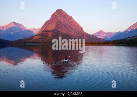 Un kayaker sul lago Swiftcurrent orologi il tramonto sul Monte Grinnell. Foto Stock