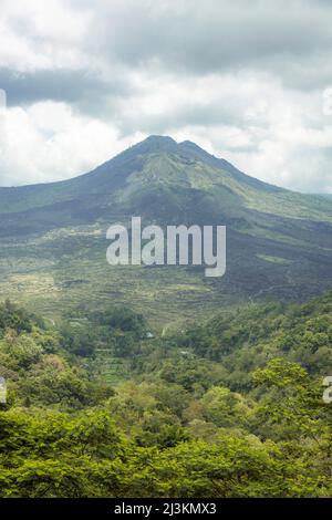 Panoramica del Monte Batur (Vulcano Kintamani) nel sud di Batur con un cielo nuvoloso e vegetazione lussureggiante; Kintamani, Bangli Regency, Bali, Indonesia Foto Stock