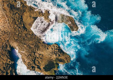 Vista presa direttamente sopra la costa rocciosa di Nusa Lembongan con le acque turchesi del Mare di Bali che si schiantano contro la riva Foto Stock
