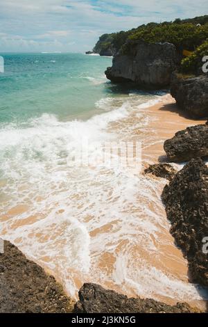 Le onde dell'oceano e la costa rocciosa con il surf che rotola sulla sabbia a Geger Beach nell'area turistica di Nusa Dua; Geger Beach, Badung, Bali, Indonesia Foto Stock