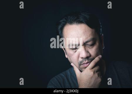 Uomo di mezza età asiatico pensiero o grave isolato su sfondo nero, Foto Stock