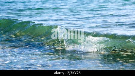 Primo piano di una piccola onda che si tuffa nel surf sulla riva con acqua limpida che mostra un fondo roccioso, Davis Bay, Sunshine Coast Foto Stock