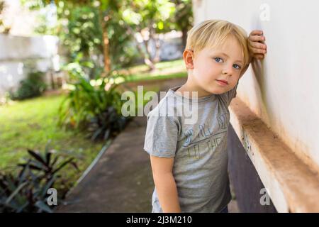 Ritratto all'aperto di un giovane ragazzo in piedi su una passerella di cemento appoggiando la testa contro la mano su un muro; Vientiane, Prefettura di Vientiane, Laos Foto Stock