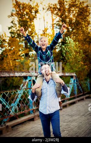 Padre che dà a suo figlio un giro in spalla in un parco in autunno; Edmonton, Alberta, Canada Foto Stock