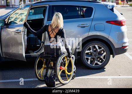 La giovane paraplegica si sposta dal veicolo alla sedia a rotelle in un parcheggio; Edmonton, Alberta, Canada Foto Stock