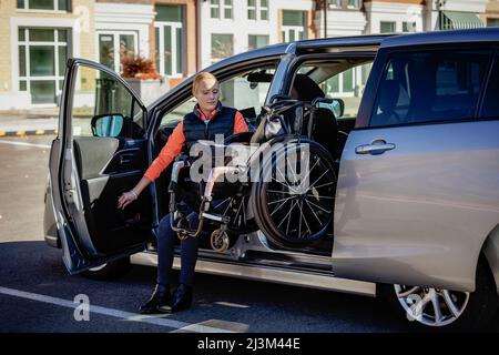 La giovane paraplegica si sposta dalla sedia a rotelle al sedile del conducente di un'auto e carica la sedia a rotelle sul sedile posteriore di un veicolo adattato Foto Stock