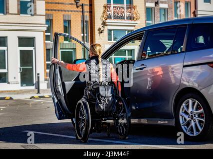 La giovane paraplegica si sposta dalla sedia a rotelle al posto di guida di un'auto in un parcheggio; Edmonton, Alberta, Canada Foto Stock