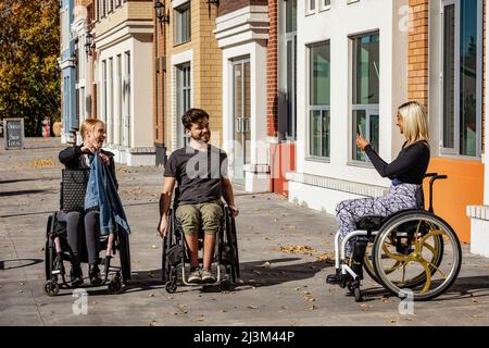 Tre giovani amici paraplegici trascorrono del tempo insieme fuori dallo shopping e scattando foto in una zona della città; Edmonton, Alberta, Canada Foto Stock