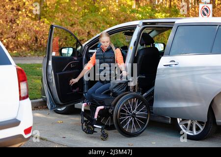 La giovane paraplegica si sposta dalla sedia a rotelle al sedile del conducente di un'auto e carica la sedia a rotelle sul sedile posteriore di un veicolo adattato Foto Stock