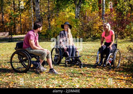 Gruppo di tre giovani paraplegici in carrozzina che visitano insieme in un parco in una bella giornata autunnale; Edmonton, Alberta, Canada Foto Stock