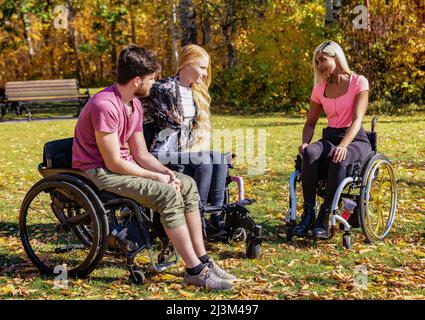 Gruppo di tre giovani paraplegici in carrozzina che visitano insieme in un parco in una bella giornata autunnale; Edmonton, Alberta, Canada Foto Stock