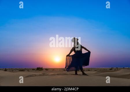 Donna con gonna lunga illuminata dal tramonto sulle sabbie desertiche; Abu Dhabi, Emirati Arabi Uniti Foto Stock