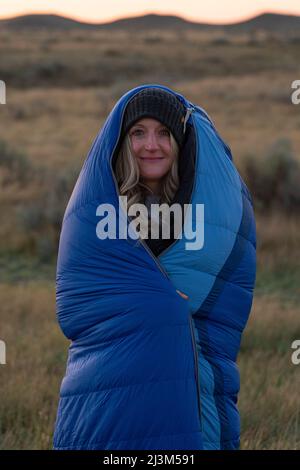 Donna avvolta in un sacco a pelo all'alba per mantenere caldo come lei si erge sul vasto paesaggio di prateria; Val Marie, Saskatchewan, Canada Foto Stock