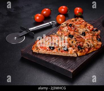 Piccola pizza fatta in casa con aggiunta di pomodori, olive ed erbe su un tavolo scuro conkrete Foto Stock