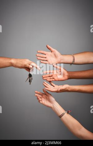 Chi vuole guidare. Studio di mani non identificabili che raggiungono per un insieme di chiavi su uno sfondo grigio. Foto Stock