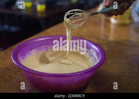 Processo di cottura delle frittelle fatte in casa: Mescolare la farina, il latte e gli ingredienti delle uova in un recipiente con una frusta Foto Stock