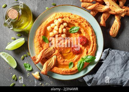 Hummus di pomodoro fresco e piccante con olive, grissini e basilico. Hummus al pomodoro servito con grissini e olio d'oliva. Foto Stock