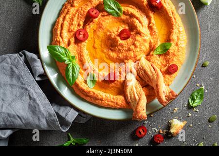 Hummus al pomodoro tradizionale e delizioso con grissini ed erbe aromatiche. L'hummus di pomodoro come uno spuntino vegano ideale. Foto Stock