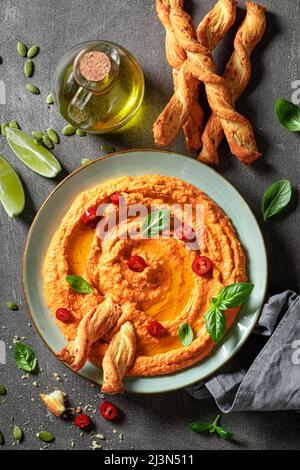 Hummus di pomodoro gustoso e fatto in casa a base di ingredienti sani. Hummus al pomodoro servito con grissini e olio d'oliva. Foto Stock