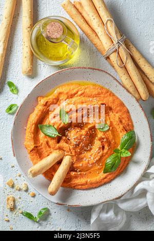 Vegano e hummus di pomodoro fatto in casa con olive, grissini e basilico. L'hummus di pomodoro come uno spuntino vegano ideale. Foto Stock