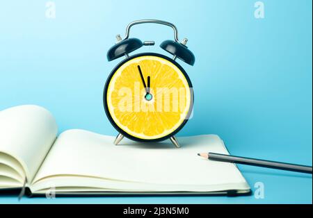 Sveglia con agrumi concetto. Limone o arancione e orologio su sfondo di colore vuoto. Vitamine, nutrizione adeguata, salute, disintossicazione, concetto di dieta. Foto di alta qualità Foto Stock