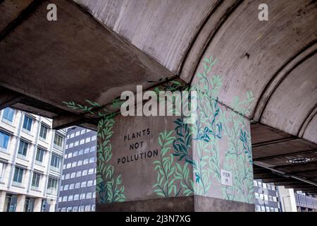 Sotto la struttura in cemento, un'opera d'arte che annuncia "piante non inquinate" è stata scritta su un pilastro del cavalcavia di Hammersmith, il 6th aprile 2022, a Londra, in Inghilterra. Foto Stock