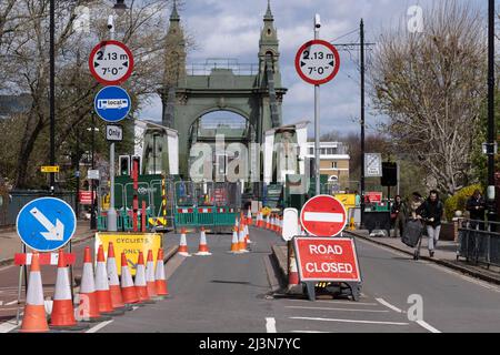 Coni e barriere bloccano l'estremità meridionale del ponte Hammersmith, chiuso al traffico automobilistico ma aperto ai pedoni a causa di problemi strutturali, il 6th aprile 2022, a Londra, Inghilterra. I controlli di sicurezza hanno rivelato "errori critici" e Hammersmith e Fulham Council hanno detto che è stato lasciato senza scelta se non chiudere il ponte di 132 anni prima che i costi di ristrutturazione possano essere soddisfatti. Nel marzo 2022, è stata approvata una nuova spesa in conto capitale di £ 3,5million per progredire nella progettazione di concept e nei lavori associati per stabilizzare la struttura di grado II. Foto Stock