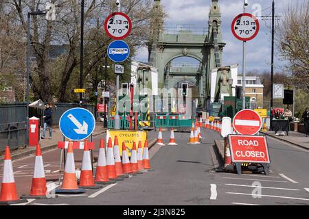 Coni e barriere bloccano l'estremità meridionale del ponte Hammersmith, chiuso al traffico automobilistico ma aperto ai pedoni a causa di problemi strutturali, il 6th aprile 2022, a Londra, Inghilterra. I controlli di sicurezza hanno rivelato "errori critici" e Hammersmith e Fulham Council hanno detto che è stato lasciato senza scelta se non chiudere il ponte di 132 anni prima che i costi di ristrutturazione possano essere soddisfatti. Nel marzo 2022, è stata approvata una nuova spesa in conto capitale di £ 3,5million per progredire nella progettazione di concept e nei lavori associati per stabilizzare la struttura di grado II. Foto Stock