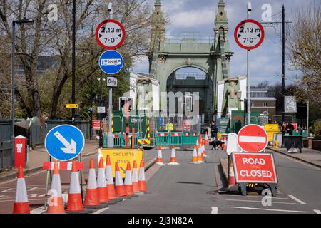 Coni e barriere bloccano l'estremità meridionale del ponte Hammersmith, chiuso al traffico automobilistico ma aperto ai pedoni a causa di problemi strutturali, il 6th aprile 2022, a Londra, Inghilterra. I controlli di sicurezza hanno rivelato "errori critici" e Hammersmith e Fulham Council hanno detto che è stato lasciato senza scelta se non chiudere il ponte di 132 anni prima che i costi di ristrutturazione possano essere soddisfatti. Nel marzo 2022, è stata approvata una nuova spesa in conto capitale di £ 3,5million per progredire nella progettazione di concept e nei lavori associati per stabilizzare la struttura di grado II. Foto Stock