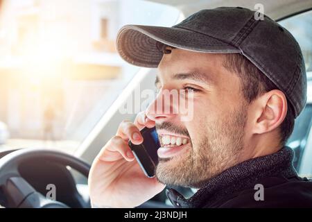 Chiamare un cliente per assicurarsi che sia a casa per una consegna. Scatto di un giovane uomo di consegna che parla su un cellulare mentre si siede in un furgone. Foto Stock