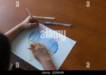 Le mani di un bambino disegnano un'icona a forma di cuore con l'immagine della bandiera nazionale dell'Ucraina. Vista dall'alto. Bambini contro la guerra. Bambini Foto Stock