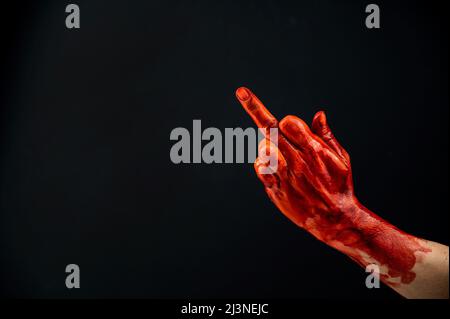 La mano femminile macchiata con sangue mostra il dito medio su uno sfondo nero. Foto Stock