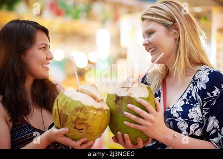 Insieme su tre. Scatto corto di due giovani donne che bevono dalle noci di cocco in un negozio di alimentari straniero. Foto Stock