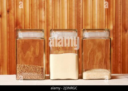 Riso, grano saraceno, semola nei vasetti di vetro trasparenti sul tavolo da cucina. Cibo rurale e cucina modello di fondo Foto Stock