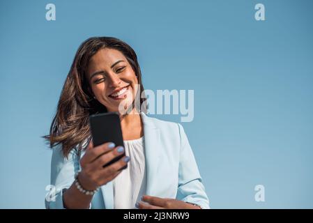 Bella felice donna d'affari latina digitando o leggendo messaggi sms online su uno smartphone. Spazio di copia Foto Stock