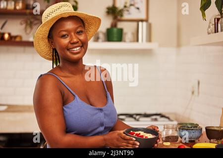 Non ho rinunciato quando le scommesse sono giù. Ritratto di una giovane bella donna che indossa un cappello mentre prepara la colazione a casa in cucina. Foto Stock