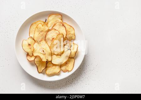 Frutta pero chips e acqua in ombra dura e soleggiata su sfondo bianco. Dessert vegano senza zucchero. Vista dall'alto. Spazio di copia. Foto Stock