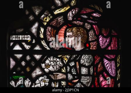 L'Arcangelo Gabriele custodisce gigli bianchi della Madonna (Lilium candidum), simbolo della castità, i suoi indumenti decorati con simboli del sole, della luna e delle stelle. Dettaglio della vetrata dell'Annunciazione degli anni '1920, Chiesa parrocchiale di Santa Maria Vergine a Shipley, West Sussex, Inghilterra. La finestra, progettata da Florence Camm (1874 - 1960) in tarda arte e mestieri o stile neogotico, è un memoriale a Etheldreda, Lady Burrell (1853-1922), che fu responsabile del restauro della chiesa parrocchiale medievale di Shipley nel 1893. Foto Stock