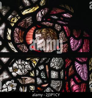 L'Arcangelo Gabriele custodisce gigli bianchi della Madonna (Lilium candidum), simbolo della castità, i suoi indumenti decorati con simboli del sole, della luna e delle stelle. Dettaglio quadrato della vetrata dell'Annunciazione degli anni '1920, Chiesa parrocchiale di Santa Maria Vergine a Shipley, West Sussex, Inghilterra. La finestra, progettata da Florence Camm (1874 - 1960) in tarda arte e mestieri o stile neogotico, è un memoriale a Etheldreda, Lady Burrell (1853-1922), che fu responsabile del restauro della chiesa parrocchiale medievale di Shipley nel 1893. Foto Stock