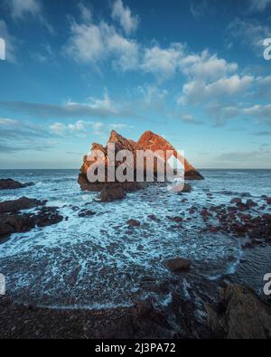 Paesaggio di arco marino naturale illuminato dal sole del tramonto. Famosa formazione rocciosa sulla costa di Moray, Highlands scozzesi, Scozia. Bow Fiddle Rock al tramonto, lunga esposizione. Foto Stock