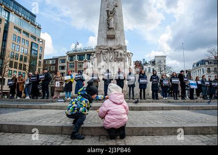 Amsterdam, Paesi Bassi. 09th Apr 2022. Due bambini piccoli sono visti guardando la gente che tiene i cartelli. Dopo i terribili eventi accaduti a Bucha (Ucraina) questa settimana, la comunità russa nei Paesi Bassi ha organizzato una veglia di dolore per commemorare le vittime delle atrocità della Federazione russa. La gente si radunò in piazza Dam indossando abiti neri e cartelli con i nomi delle città ucraine attaccate dall'esercito russo. L'evento è stato un'azione di lutto silenzioso senza annunci o discorsi. Credit: SOPA Images Limited/Alamy Live News Foto Stock