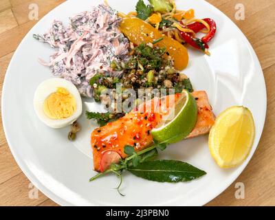 Un piatto di filetto di salmone al peperoncino dolce e varie insalate. Foto Stock