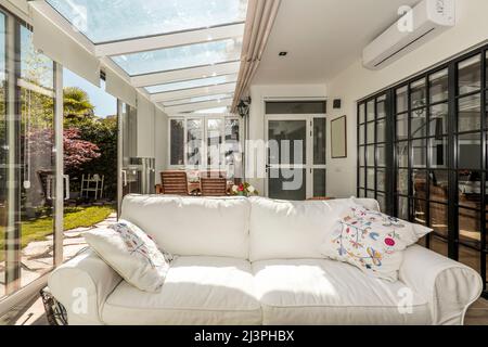 Terrazza in vetro e alluminio con grandi porte scorrevoli, mobili in legno e un grande divano bianco Foto Stock