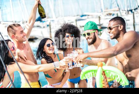 Amici alla moda che si divertono a tostare vino champagne al party in barca a vela - amicizia e concetto di stile di vita di viaggio con persone multiculturali Foto Stock