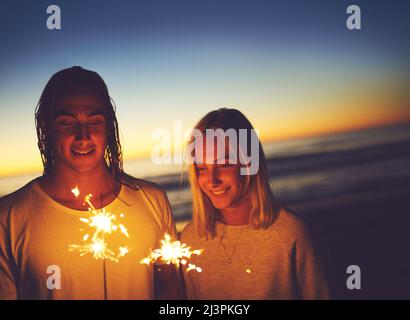 Festeggia la notte. Scatto di una giovane coppia che gioca con i luccicanti sulla spiaggia di notte. Foto Stock