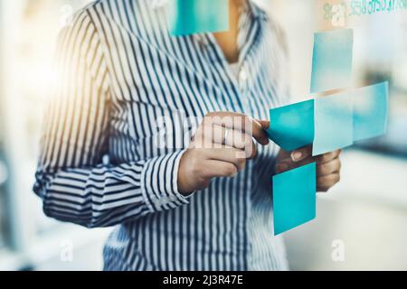 Metta le vostre idee avanti e guardi il successo accadere. Primo piano di un'irriconoscibile donna d'affari che aderisce note adesive su una parete di vetro in un ufficio. Foto Stock